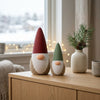Coppia di Gnomi DEKO in ambientazione Japandi Hygge: Su credenza in legno con vasetto di pino ed atmosfera natalizia.