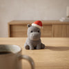 Ippolito in Grigio, ippopotamo a maglia col cappello di Natale, su un tavolo in legno chiaro
