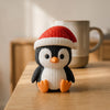 Frac in Classico, pinguino a maglia col cappello di Natale, su un tavolo in legno chiaro